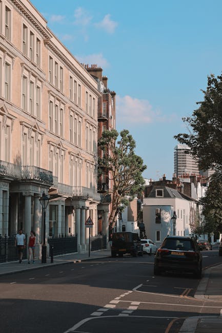 A quiet residential street in Kentish Town lined with rows of Victorian-style terraced houses, featuring white facades, bay windows, and tiled roofs under an overcast sky. The pavement runs alongside